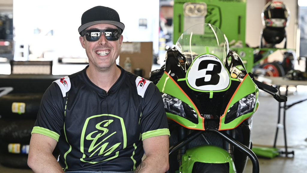 Late powersports enthusiast Scott Mullin wearing sunglasses and smiling in front of his motorcycle